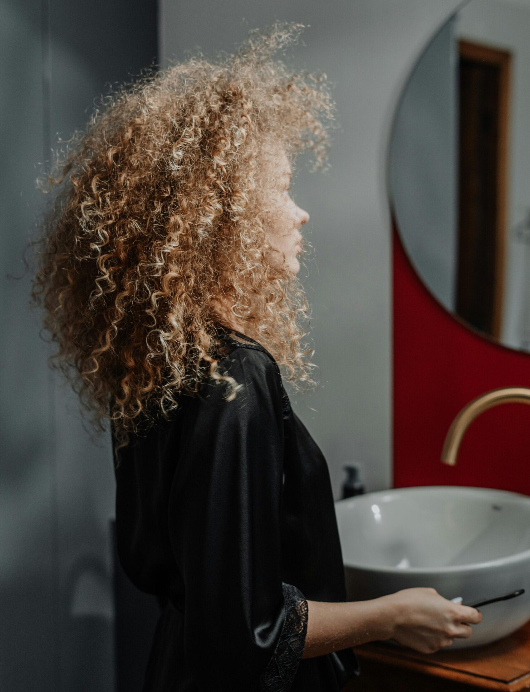 Kvinne i morgenkåpe ser inn i speilet på badet, i et øyeblikk av refleksjon og egenomsorg – symbol på bevissthet rundt trygg bruk og vedlikehold av sexleketøy.