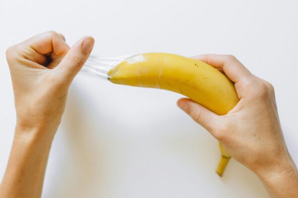 Hender som trekker en kondom av en banan, symboliserer viktigheten av å bruke beskyttelse på dildoer for trygg og hygienisk bruk.