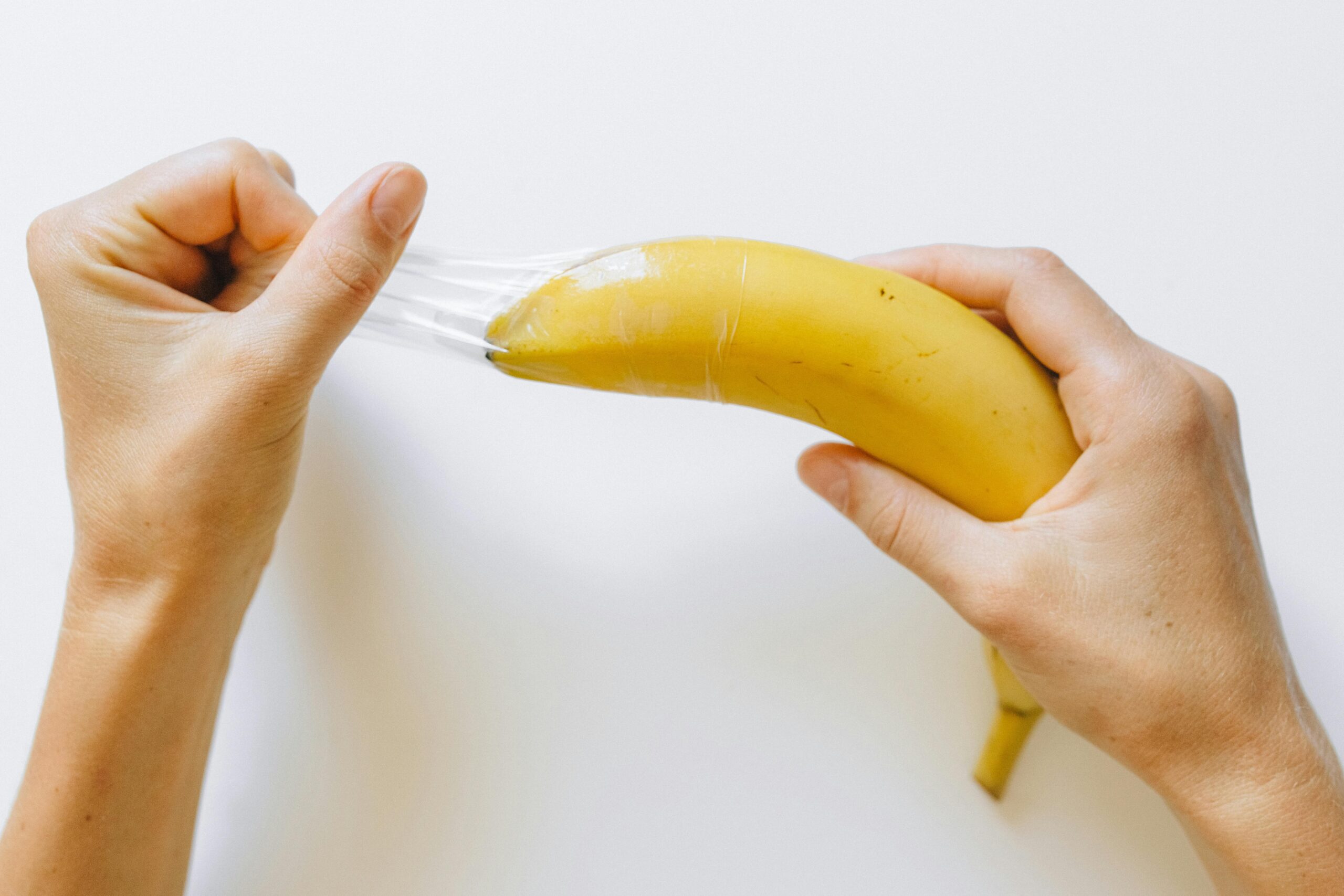 Hender som trekker en kondom av en banan, symboliserer viktigheten av å bruke beskyttelse på dildoer for trygg og hygienisk bruk.