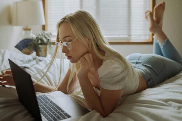 Kvinne ligger avslappet i sengen med en laptop, og undersøker sexleketøy på nett – et symbol på trygghet, kunnskap og bevisste valg.
