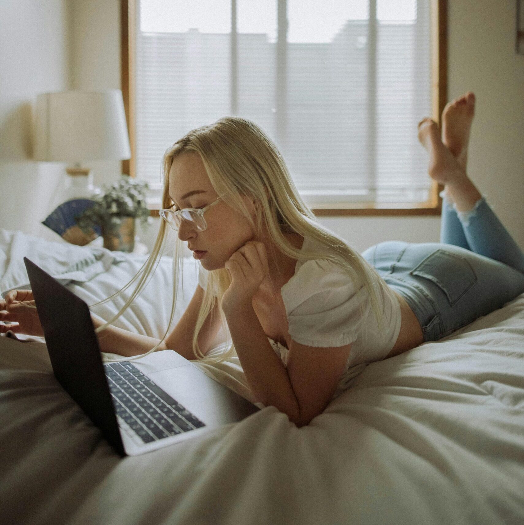 Kvinne ligger avslappet i sengen med en laptop, og undersøker sexleketøy på nett – et symbol på trygghet, kunnskap og bevisste valg.