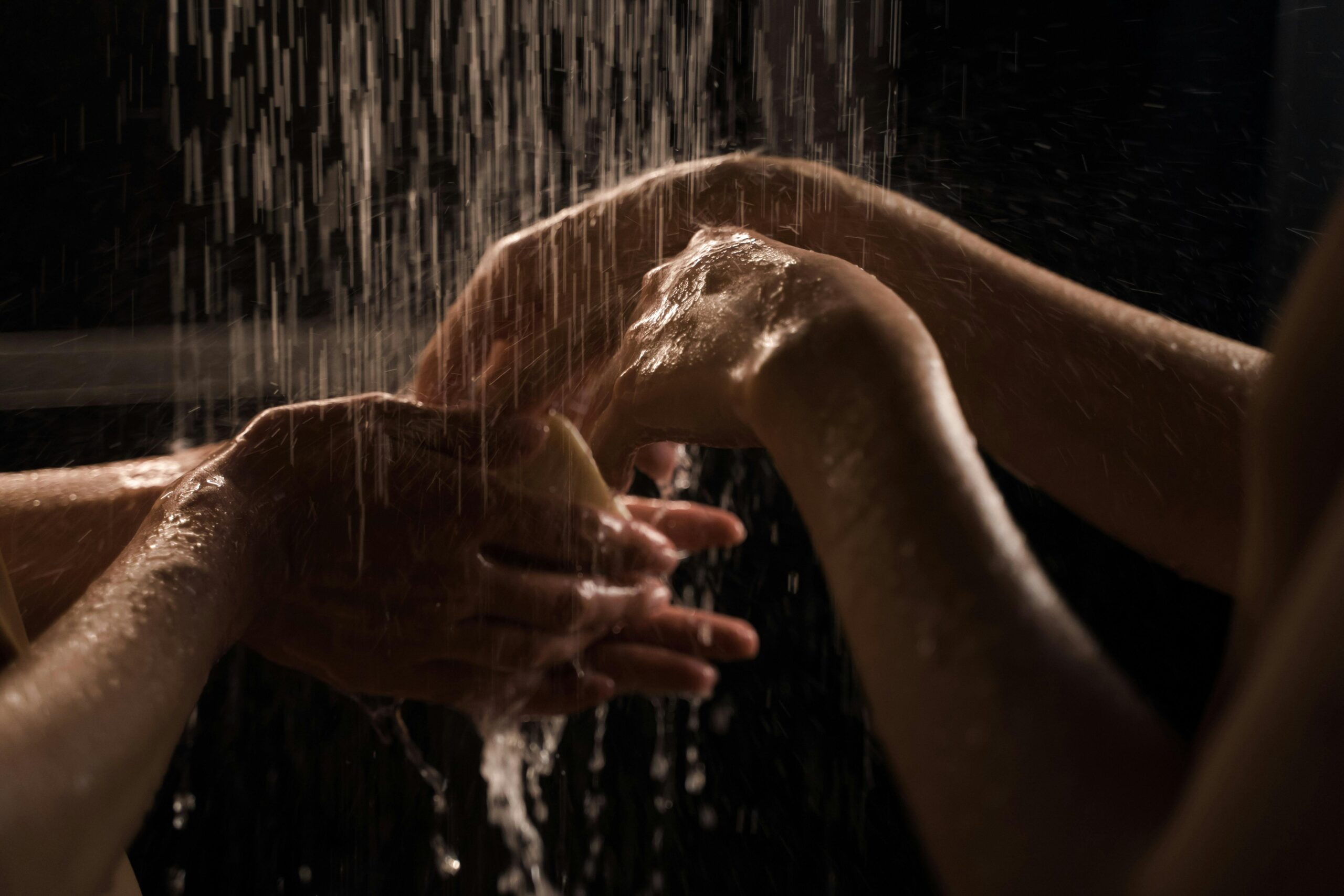 To hender som vaskes under dusjstråle – symboliserer rengjøring og hygiene ved bruk av sexleketøy som dobbeldildo.