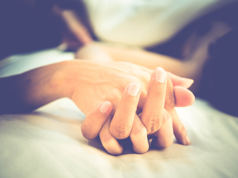 To hender som holder hverandre i sengen – et symbol på intimitet, trygghet og nærhet i parforhold, relevant for artikkel om å bruke dildo sammen med partner.