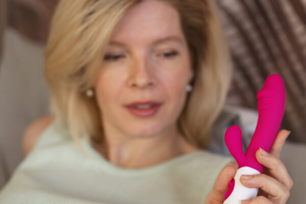 Kvinne ser vurderende på en rosa rabbit dildo med strukturert og roterende skaft – illustrerer valg av vibrator med ekstra funksjoner for G-punktstimulering.