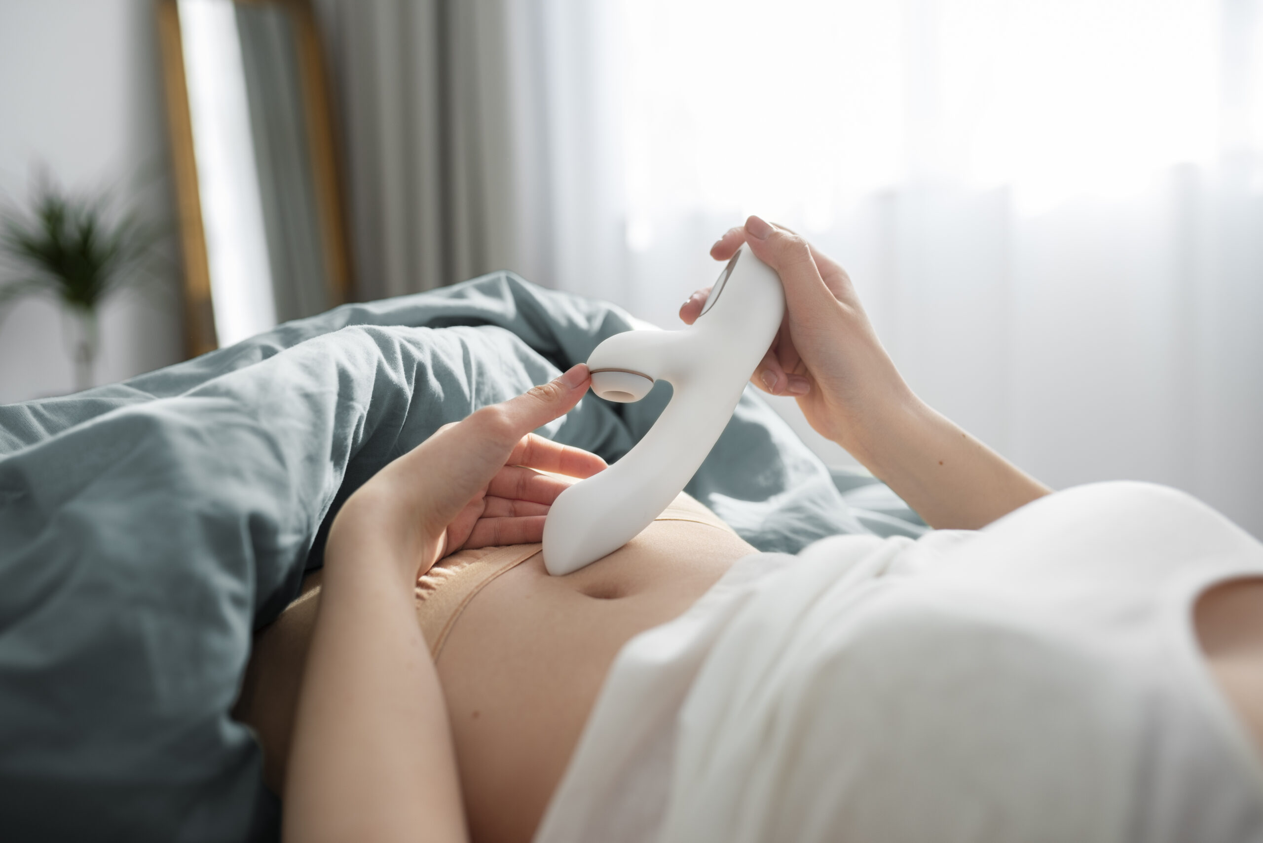Person som ligger i sengen og utforsker en hvit rabbitvibrator med sugefunksjon – viser tydelig lufttrykksåpningen for klitorisstimulering.