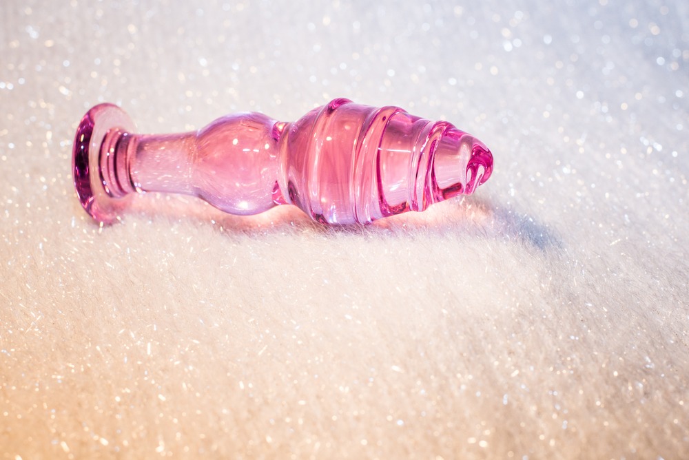 Rosa glassdildo med tydelig base og spiralform, liggende på mykt, hvitt underlag.